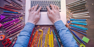Corporate Design – Hände liegen auf einem Laptop, um den Laptop liegen farbige Stifte